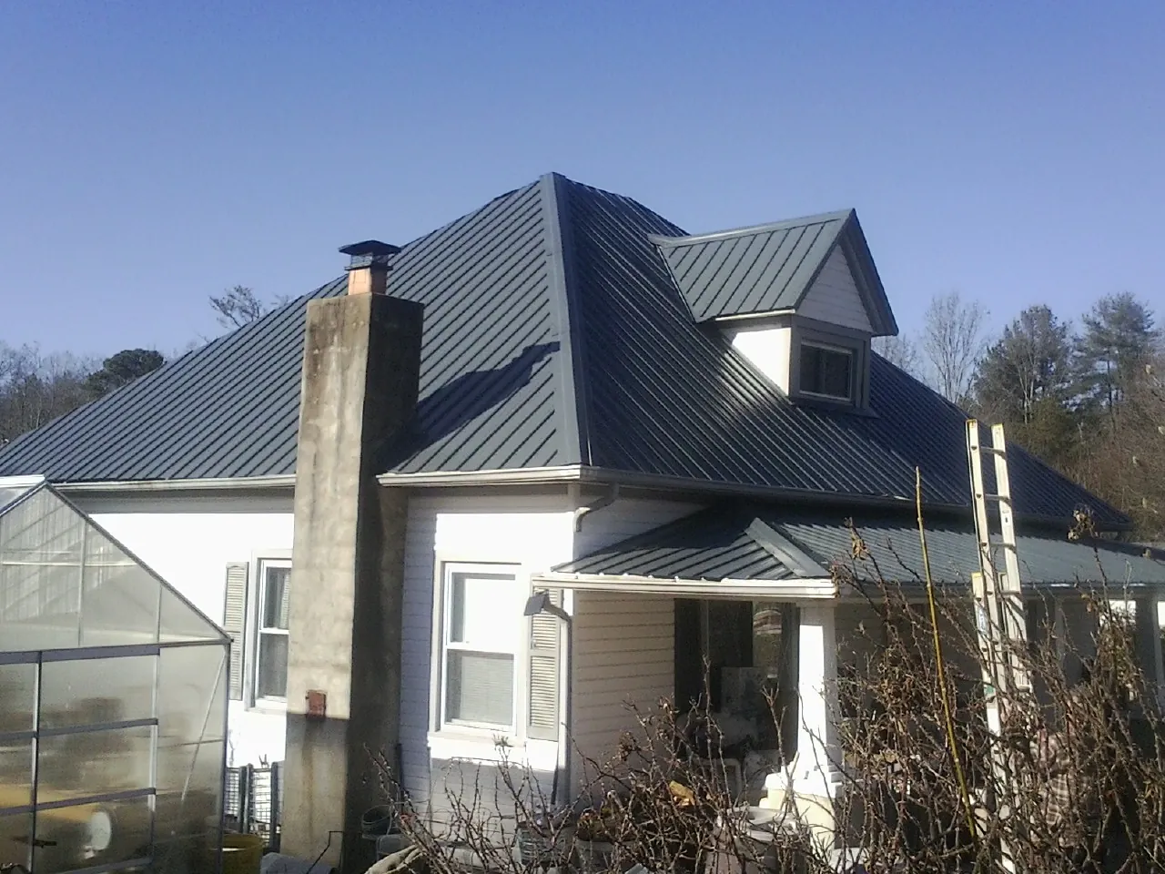 Dark blue standing seam metal roof on a white farmhouse with dormer — Slate & Tile Roof Repair by Roofing Brothers in Putnam Station