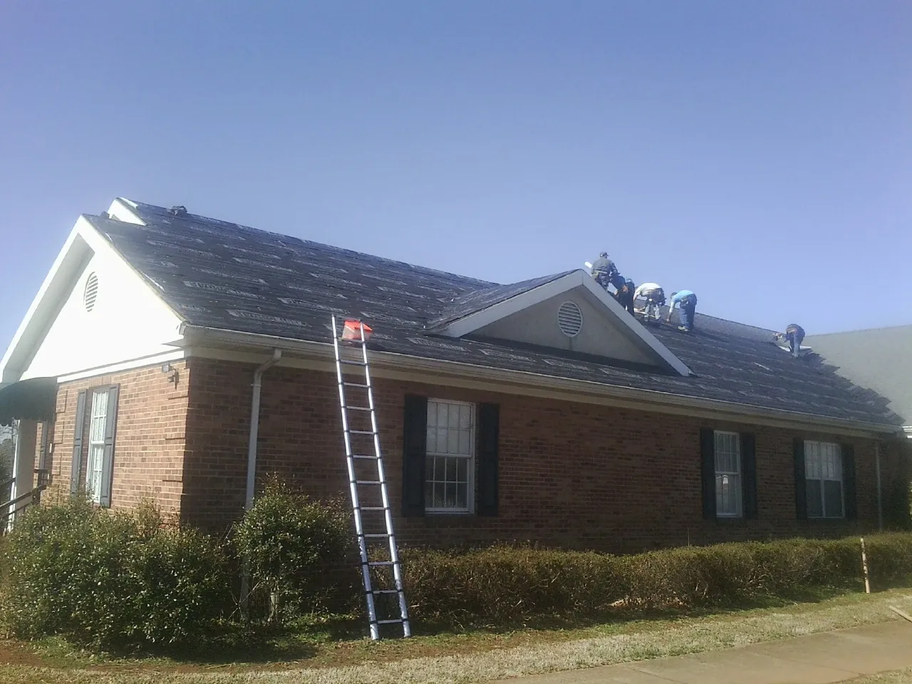 Crew tearing shingles off a brick ranch roof with a ladder set — Emergency Roof Repair work by our crew in Putnam Station