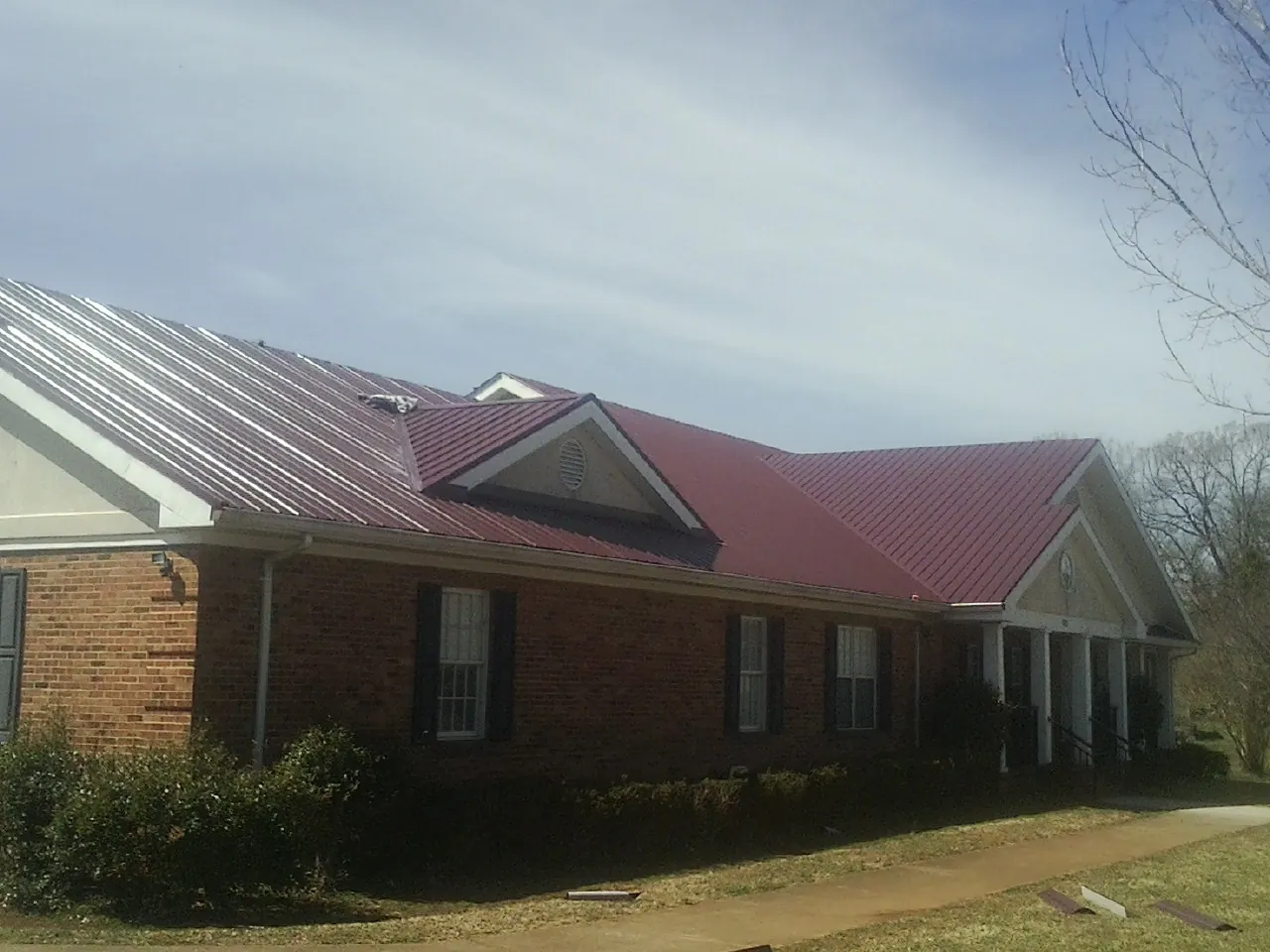 Red metal roof with gabled entries on a long brick building, from a Hail Damage Roof Repair job in Putnam Station