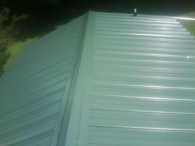 New green metal panels meeting at the ridge of a roof — Flat Roof Repair work by our crew in Putnam Station