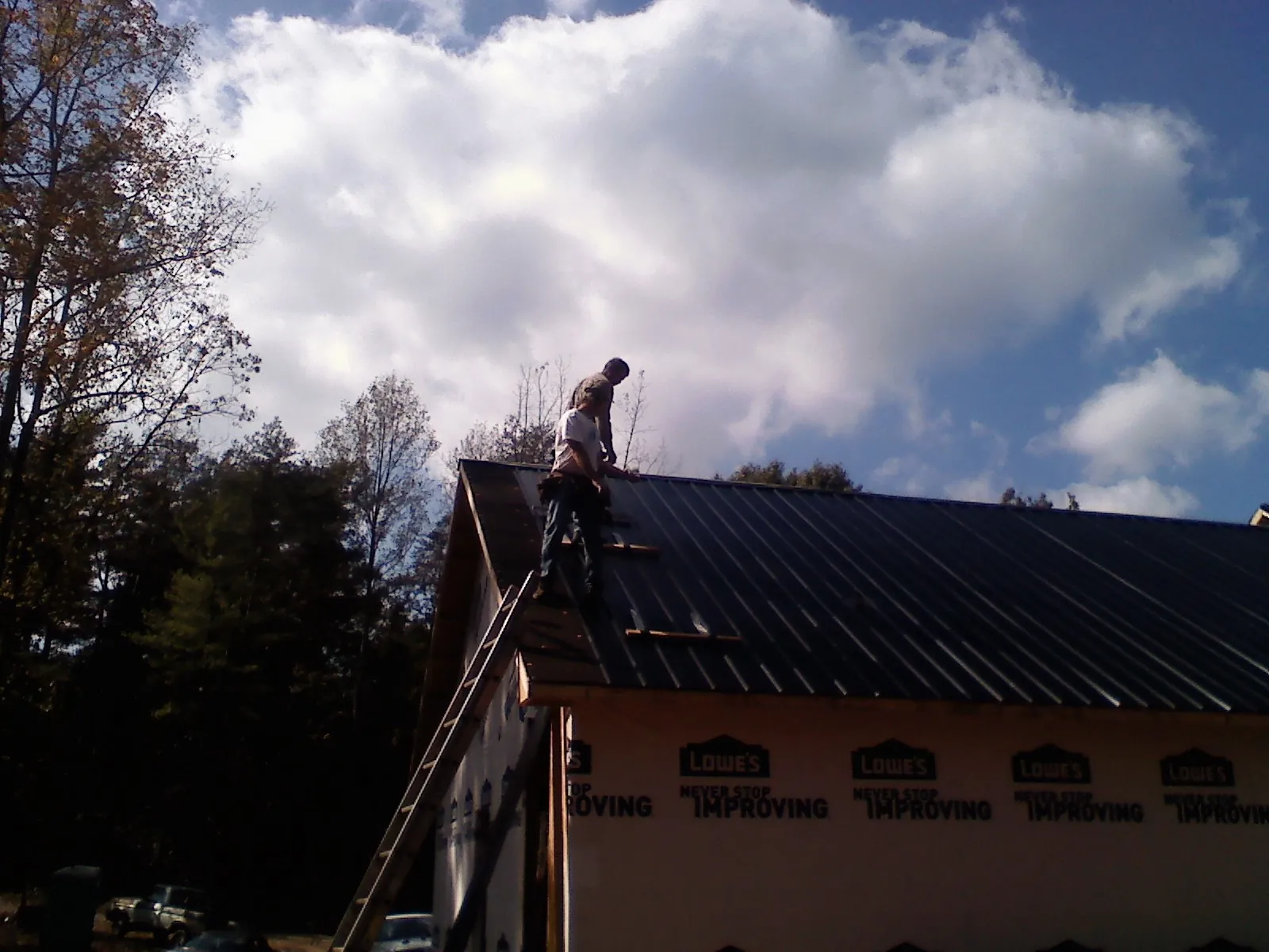 Roofer fastening dark metal panels high against a cloudy sky, from a Roof Inspection job in Putnam Station