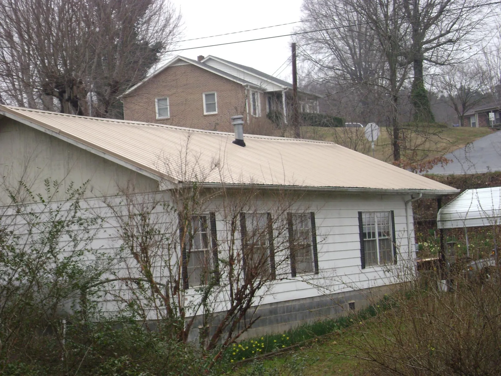Tan metal roof on a white sided house set into a hillside — Commercial Roofing by Roofing Brothers in Putnam Station