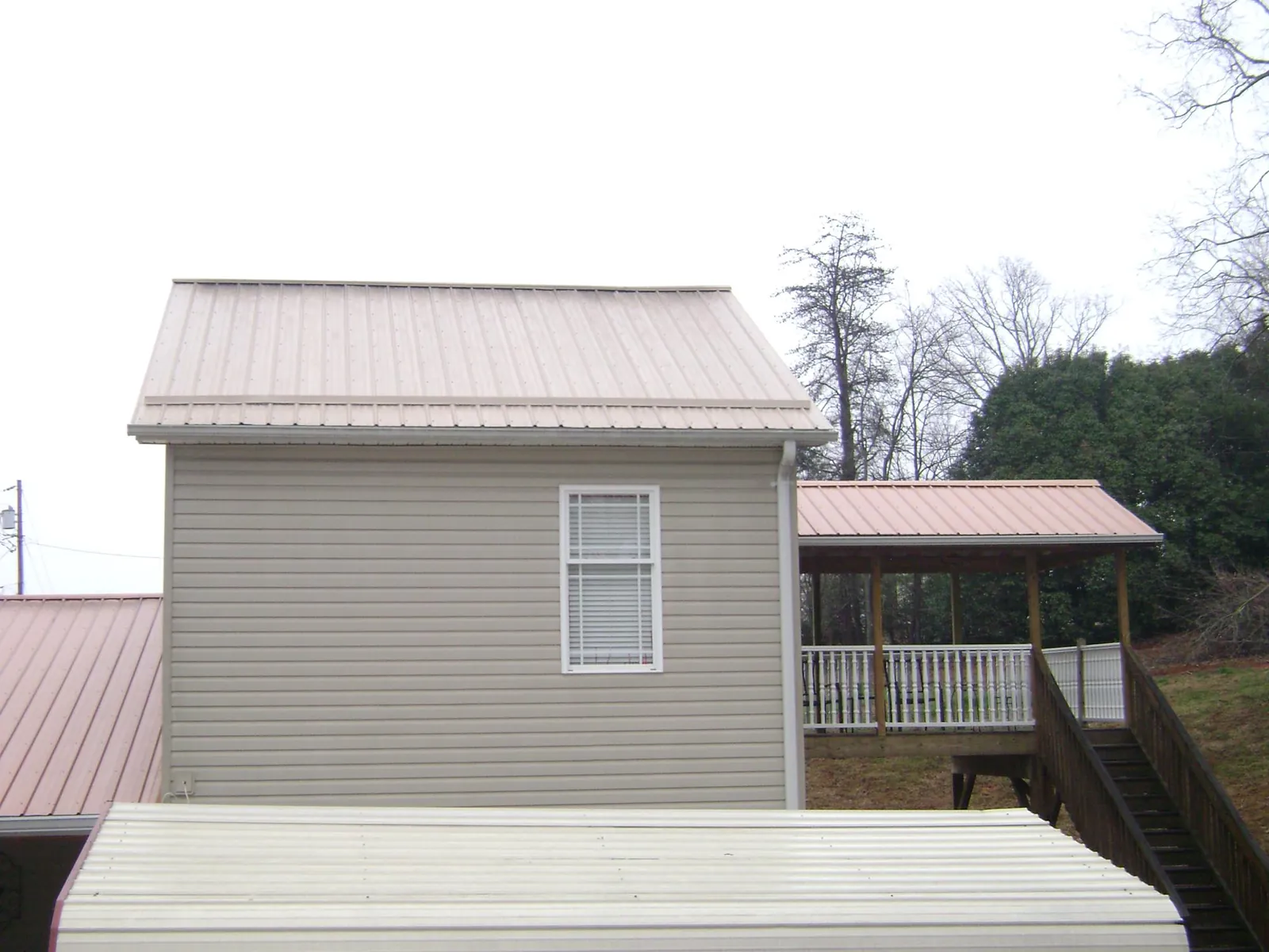 Tan metal roofs on a two story addition and attached porch, from a Roof Replacement job in Putnam Station